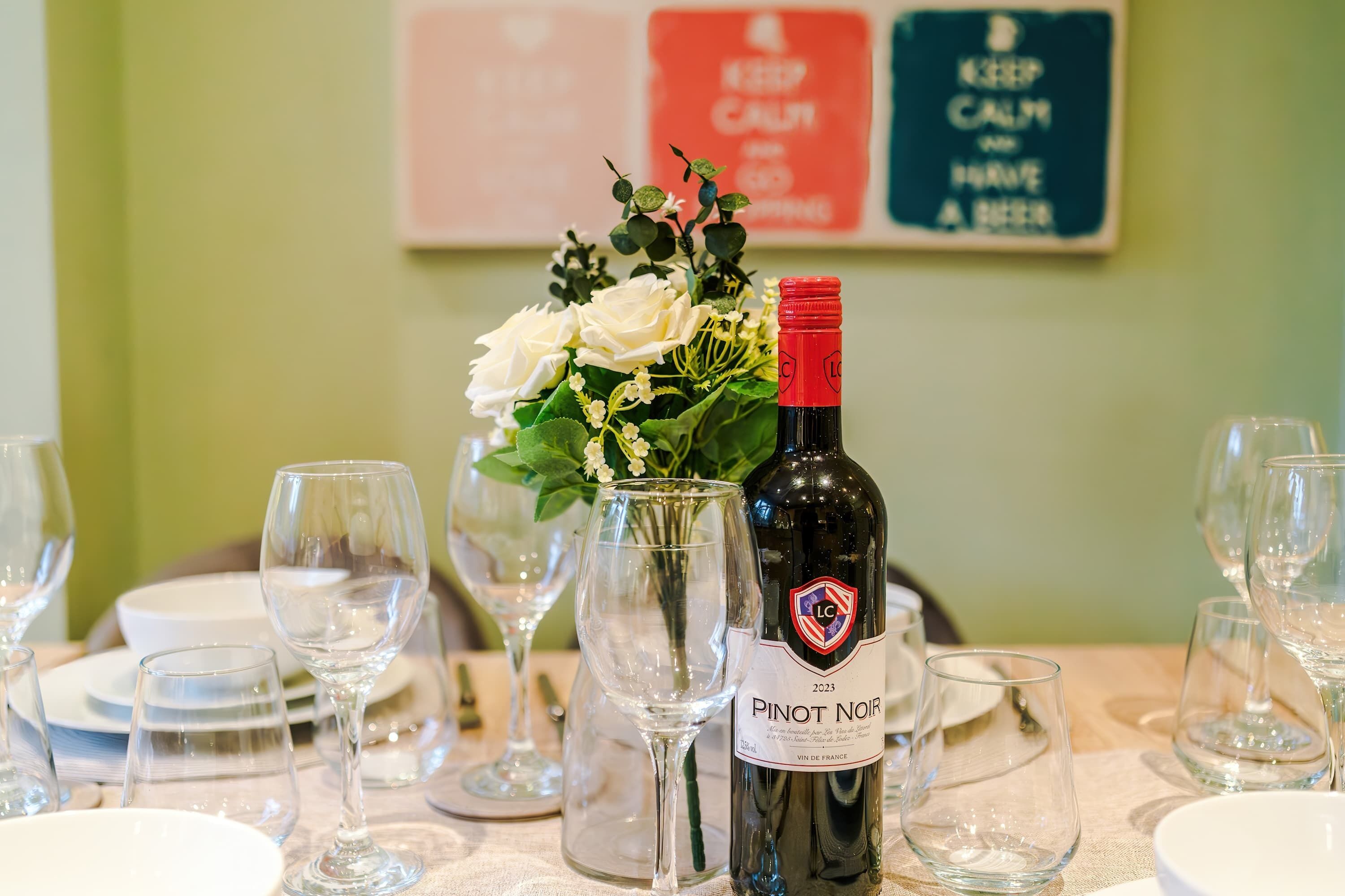 A dining table set with wine glasses, a bottle of Pinot Noir, and a vase with white flowers.
