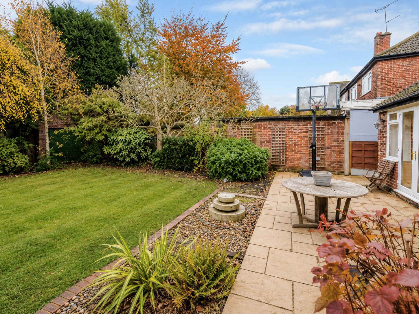 A backyard with a lawn, a brick wall, and a patio area with a table and chairs.