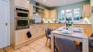 A modern kitchen with two ovens, a stove, and a dining area with a table set for four. - 5BR Contractor House | Free Parking | Near Airport (Manchester)