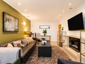 A modern living room with a sofa, coffee table, and a fireplace. - 5BR Contractor House | Free Parking | Near Airport (Manchester)