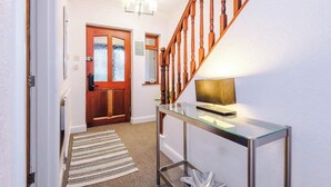 A hallway with a wooden staircase, a glass console table with a lamp, a patterned rug, and a door with frosted glass panels. - 5BR Contractor House | Free Parking | Near Airport (Manchester)