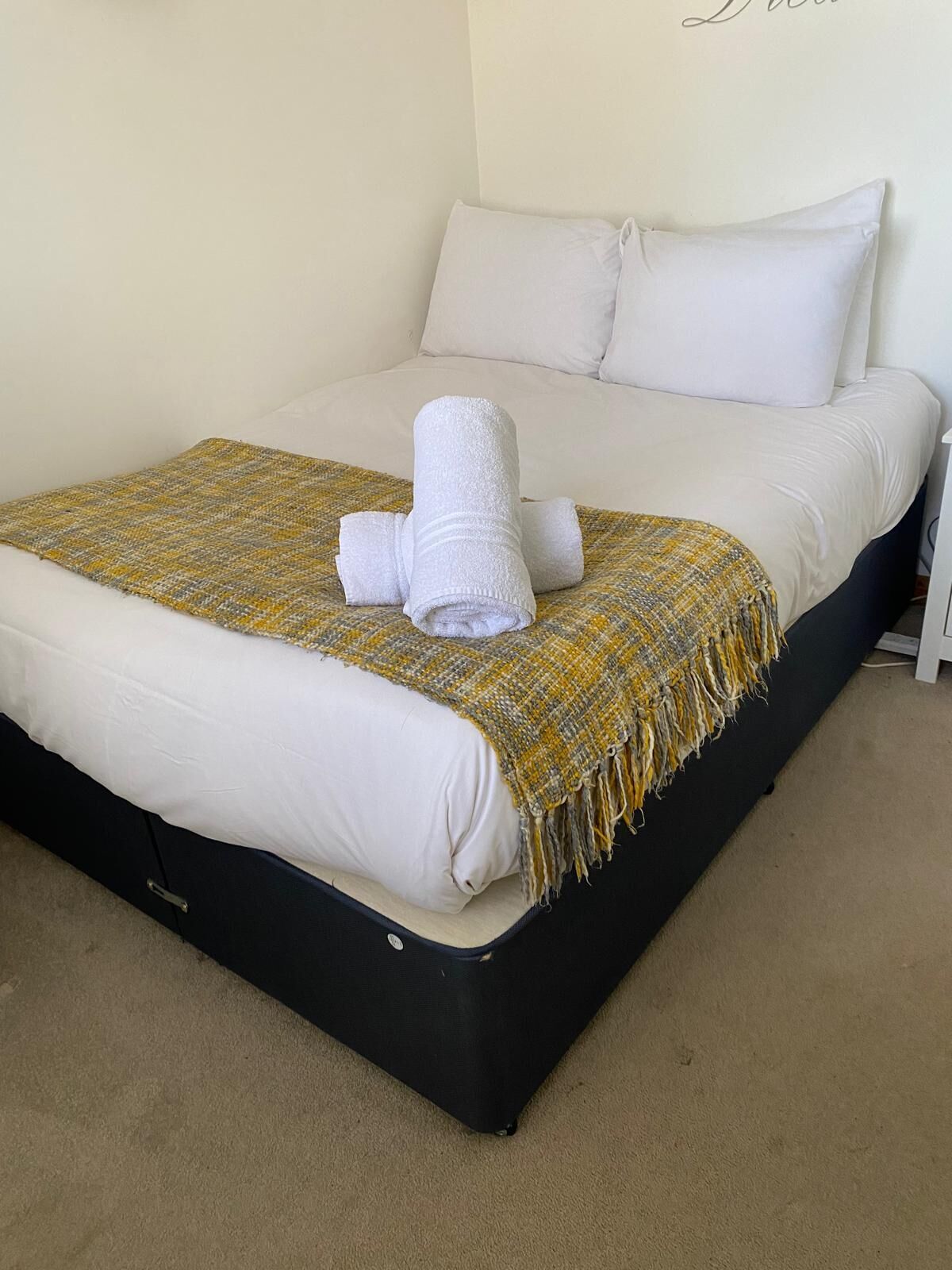 A neatly made bed with a white duvet, a yellow and gray woven throw blanket, and a rolled white towel on the bed.