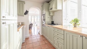 Une cuisine étroite avec des meubles de couleur vert clair, un plan de travail en bois et une fenêtre équipée de stores.