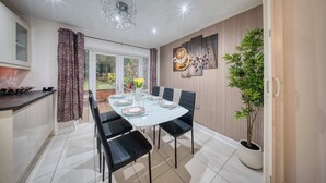 Ein Essbereich mit einem weißen Tisch, gedeckt für vier Personen, schwarzen Stühlen, einer Kristallleuchtreibe und einem Blumentopf.
