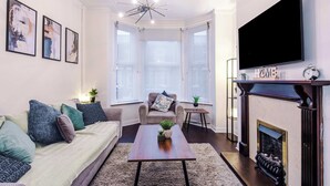 Ein Wohnzimmer mit Sofa, Couchtisch, Kamin, Fernseher und Kunstwerken an der Wand.