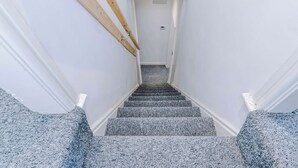 Escada com corrimão de madeira e degraus revestidos a carpete, levando a uma porta.