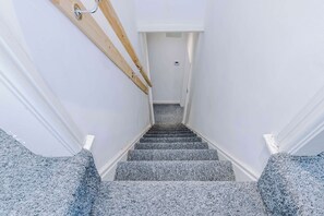 A staircase with a wooden handrail and carpeted steps leading to a door. - 3 bedroom town house - Etihad Stadium - Free Parking (Manchester)