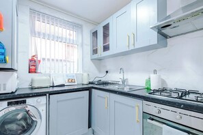 A kitchen with a washing machine, a toaster, a kettle, a sink, and a gas stove. - 3 bedroom town house - Etihad Stadium - Free Parking (Manchester)