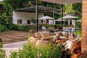 Un patio al aire libre con un área de estar techada, una piscina y abundante vegetación.