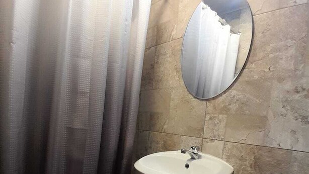 A bathroom with a shower curtain, a sink, a toilet, and a mirror. - amalfi surf lodge  (Chiltiupan)