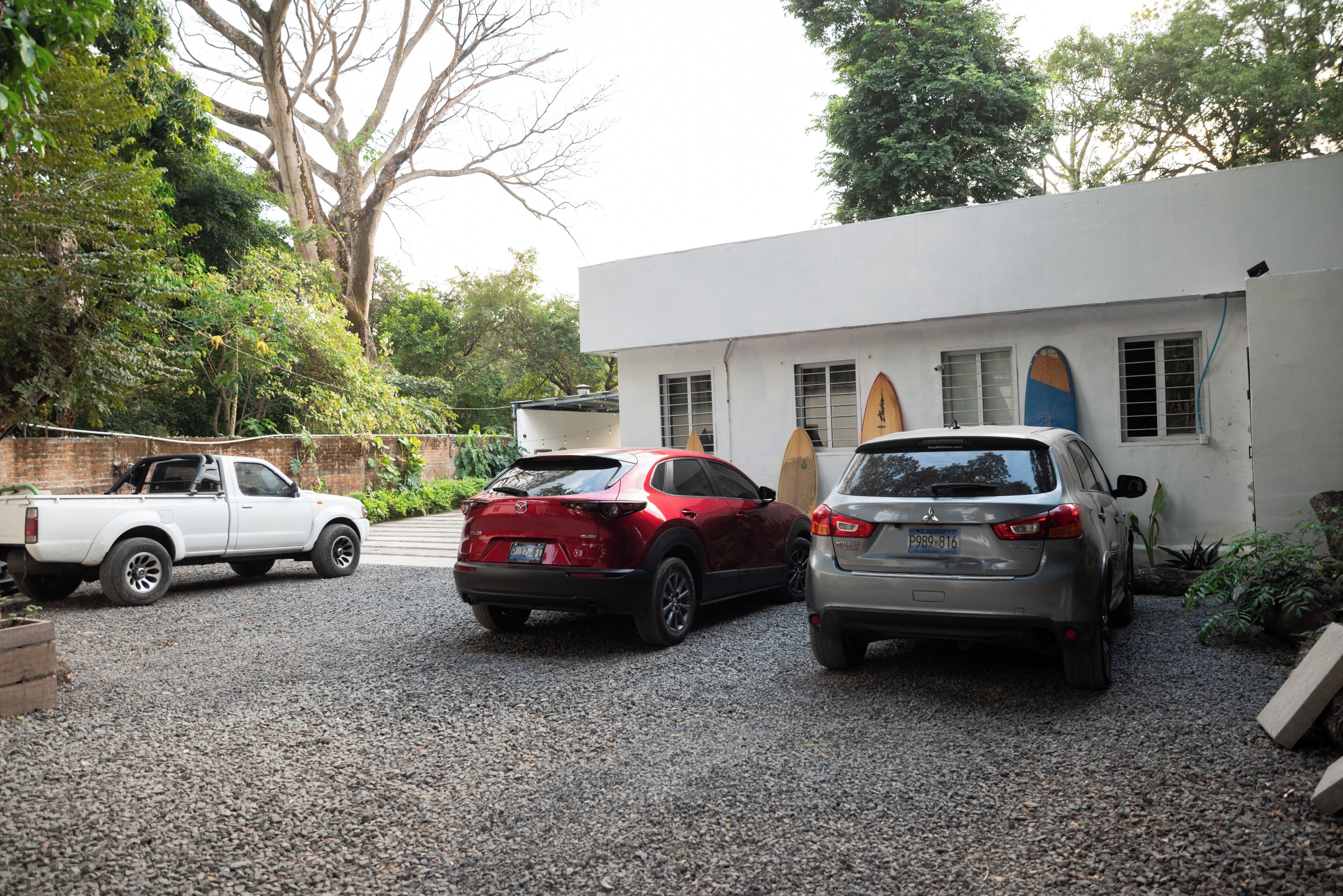 A gravel driveway with three parked vehicles, a white pickup truck, a red SUV, and a silver sedan.