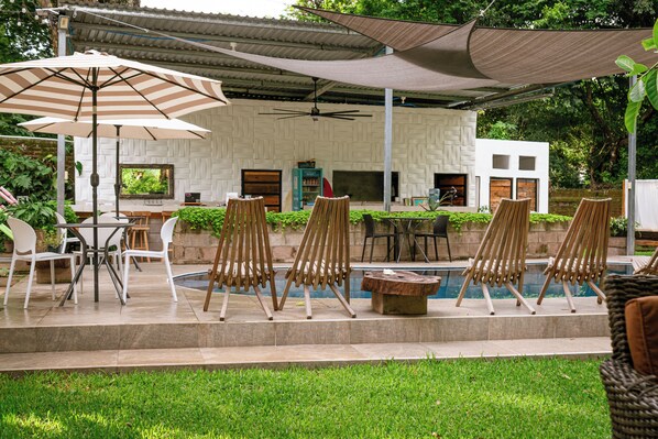 An outdoor seating area with tables and chairs, a pool, and a covered patio with a fan. - amalfi surf lodge (Chiltiupan)