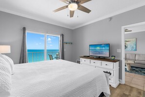 A bedroom with a large bed, a TV, a ceiling fan, a balcony with a view of the ocean, and a painting on the wall. - Crystal Shores West Beachfront 2 Bed. Indoor/Outdoor Pool. Free Daily Activities (Gulf Shores)