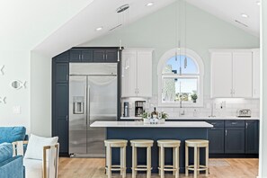 A modern kitchen with a large island, dark cabinets, stainless steel appliances, and a view of the city. - Ocean Chateau (Sneads Ferry)