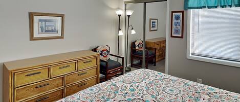 Een slaapkamer met een bed, een dressoir, een stoel en een spiegel.