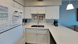 Una cocina compacta con armarios blancos, un lavamanos de acero inoxidable y una cafetera.