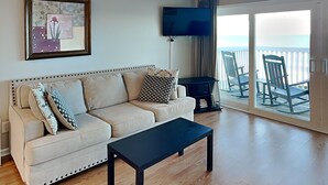 Una sala de estar con sofá, mesa de centro, televisor y balcón con sillas.