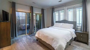 Una camera da letto con un letto, un comodino, una TV e una porta scorrevole in vetro che dà su uno spazio all'aperto.
