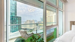 Ein modernes Hotelzimmer mit großen Fenstern, einem Balkon mit Korbstühlen und Blick auf die Stadtlandschaft.