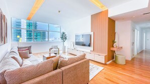 Ein modernes Wohnzimmer mit einer großen Couch, einem flachbildfernseher an einer Holzvertäfelung und einem großen Fenster mit Blick auf die Stadt.