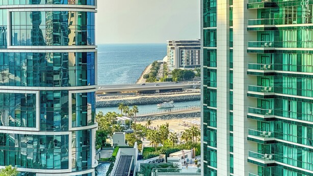 Ein modernes Gebäude mit spiegelnden Glasfenstern, Blick auf das Meer und einen Strand im Hintergrund.