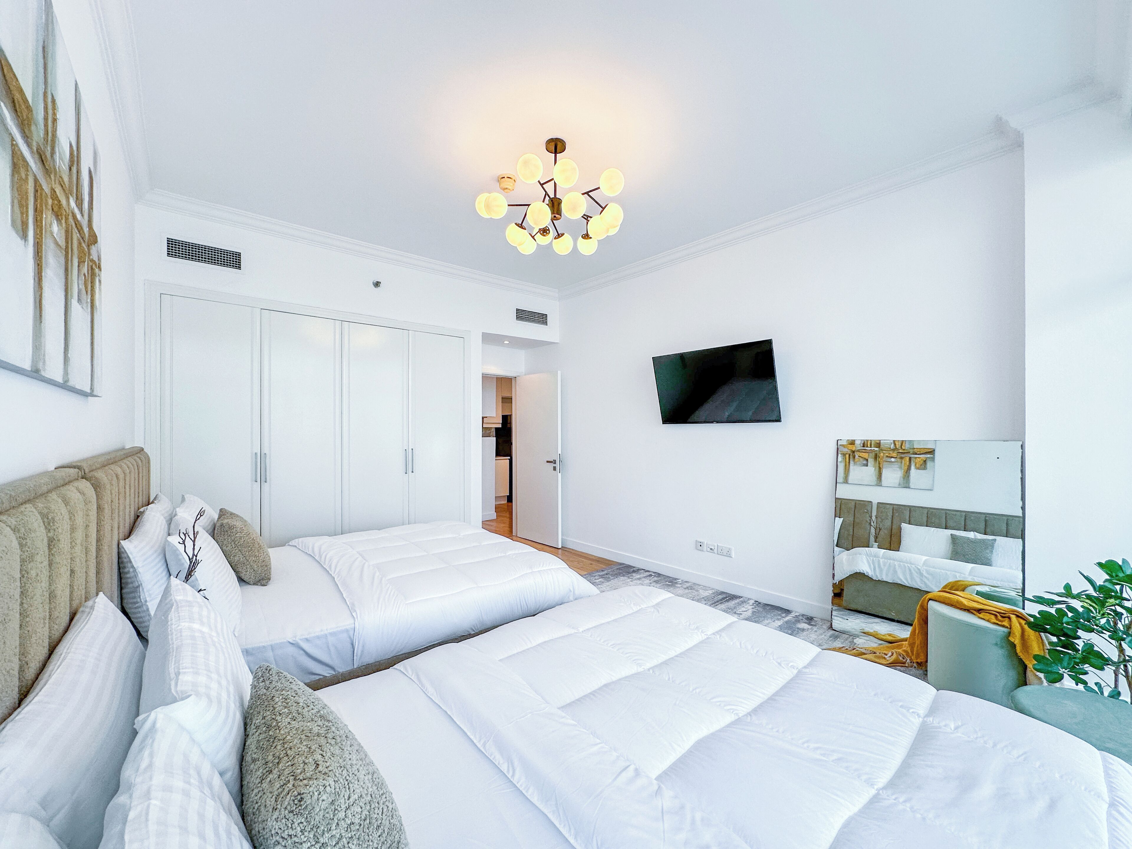 A modern bedroom with two beds, a TV, and a wardrobe.