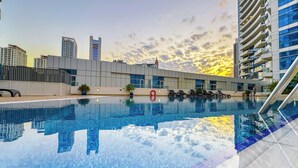 Ein Schwimmbecken mit Stadtansicht im Hintergrund, darunter moderne Gebäude und ein Sonnenuntergang.