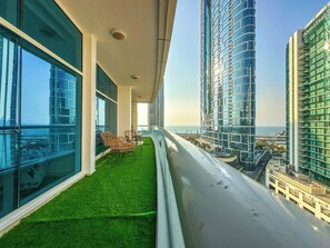 Ein Balkon mit Meerblick, möbliert mit Korbstühlen, und mit Blick auf eine Stadtlandschaft mit hohen Gebäuden.