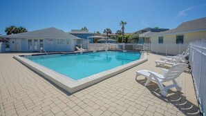 Une piscine rectangulaire avec une terrasse carrelée, entourée de chaises longues blanches et d’une clôture blanche.