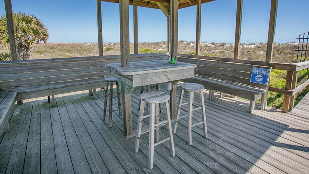 Une terrasse en bois avec une table et des tabourets, un panneau d’information sur les tortues marines et une vue sur la plage.