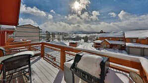 Un balcón cubierto de nieve con mobiliario exterior, con vistas a un paisaje nevado y edificios.