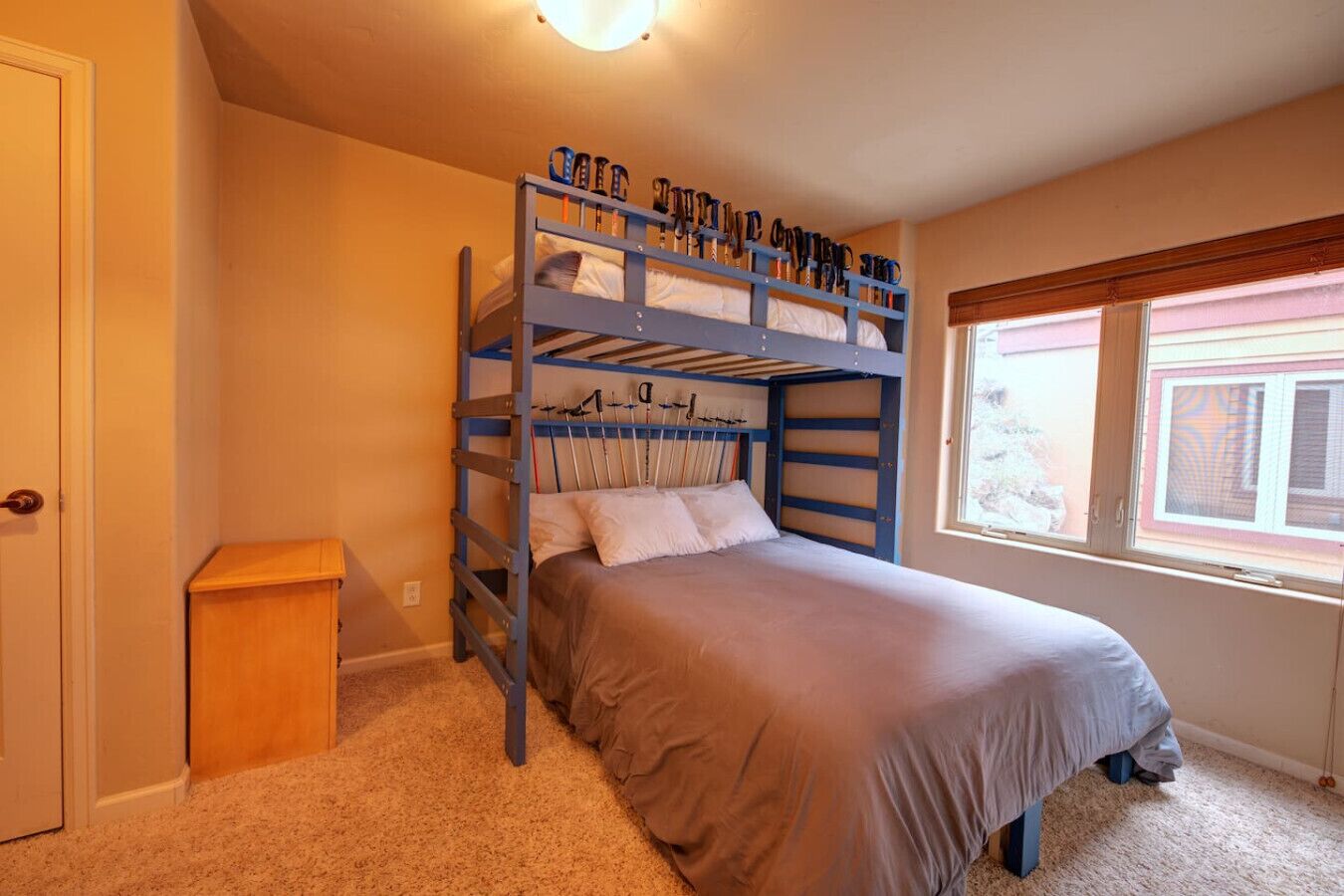 A bunk bed room with a window, carpeted floor, and a small wooden cabinet.