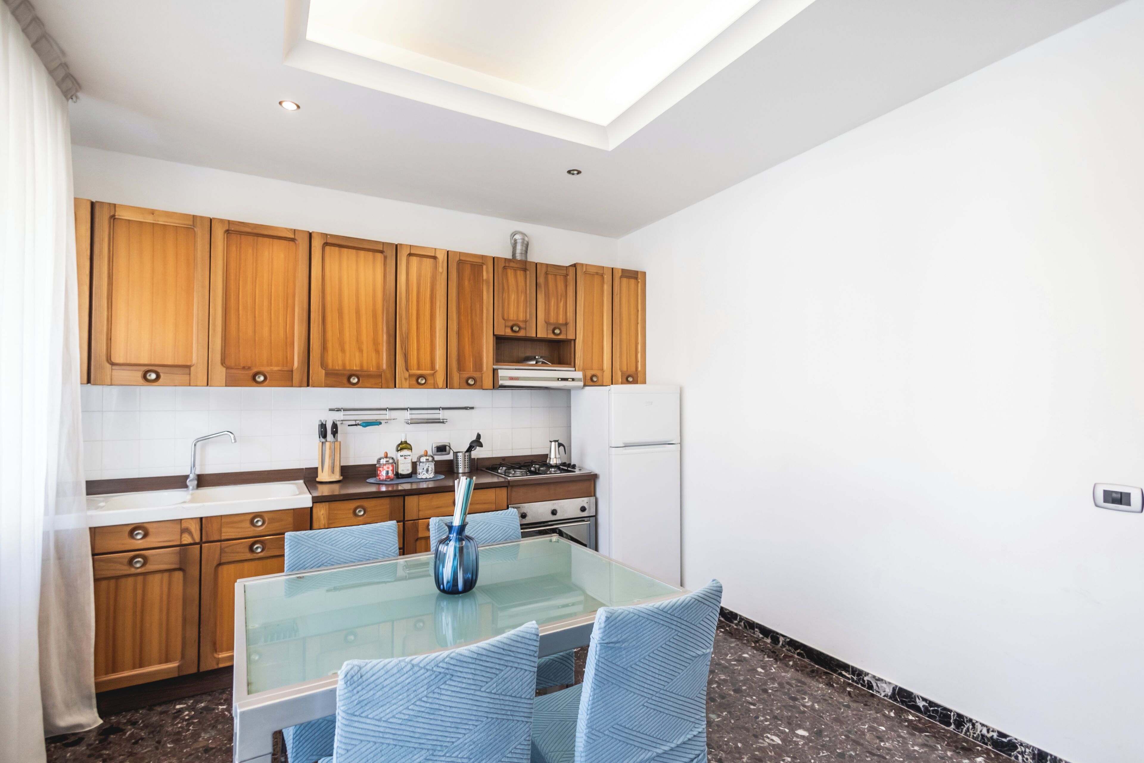 A modern kitchen with wooden cabinets, a glass dining table, and a skylight.