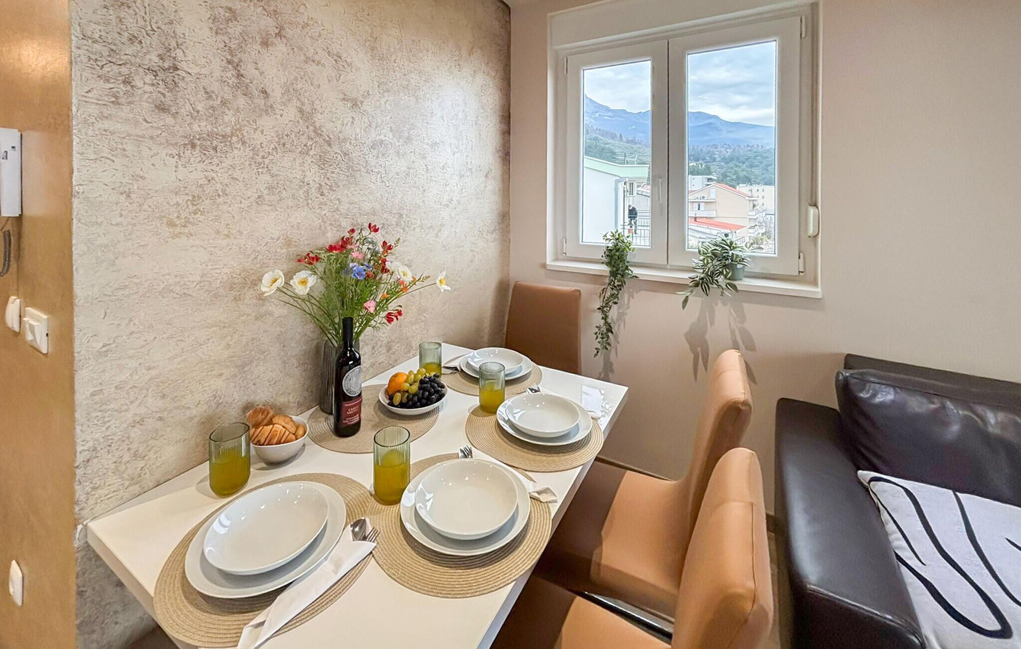 A dining area with a table set for four, a vase with flowers, and a view of mountains through the window.