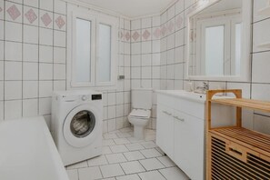 Un bagno compatto con lavatrice, water e ripiano in legno.