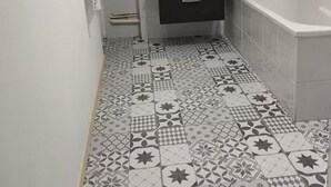 Une salle de bain avec un sol carrelé, un meuble-lavabo noir, un miroir et une douche.