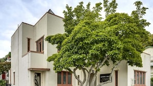 Un edificio de dos pisos con fachada blanca, un árbol en frente y un cartel que dice "CAFE & LAVABO".