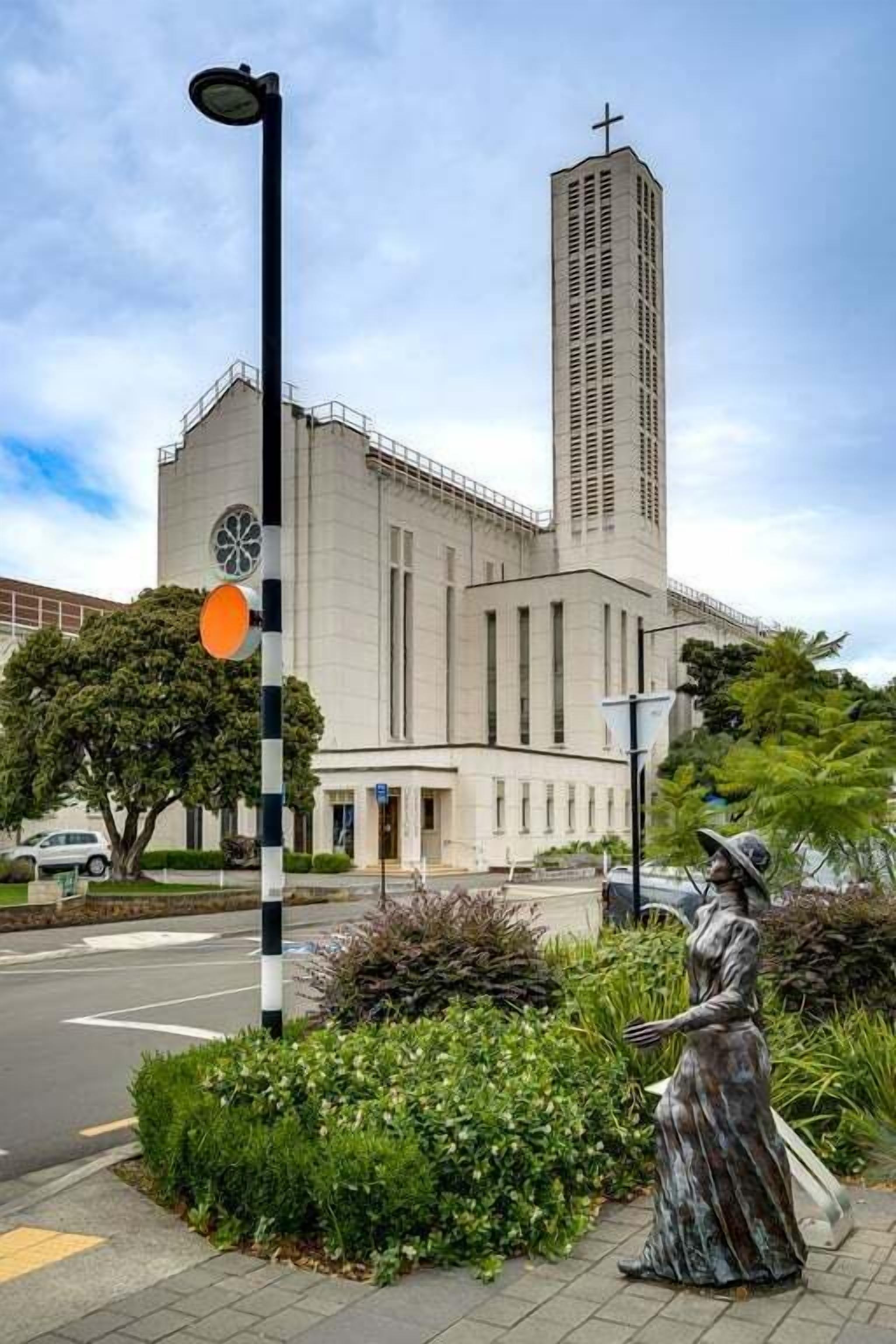A church with a tall tower and a statue of a woman on the sidewalk.
