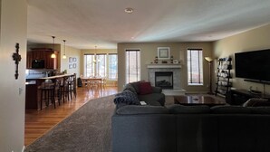 A spacious living room with a fireplace, a television, and a bookshelf. - Spacious 5-bedroom house in Olathe. Finished basement and outdoor deck/space. (Olathe)