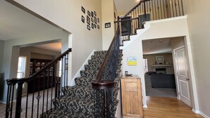 A staircase with a patterned carpet and dark railings leading to a second floor. - Spacious 5-bedroom house in Olathe. Finished basement and outdoor deck/space. (Olathe)