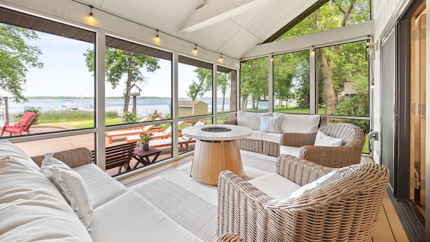 A covered outdoor seating area with wicker furniture, a round table, and a view of the lake.