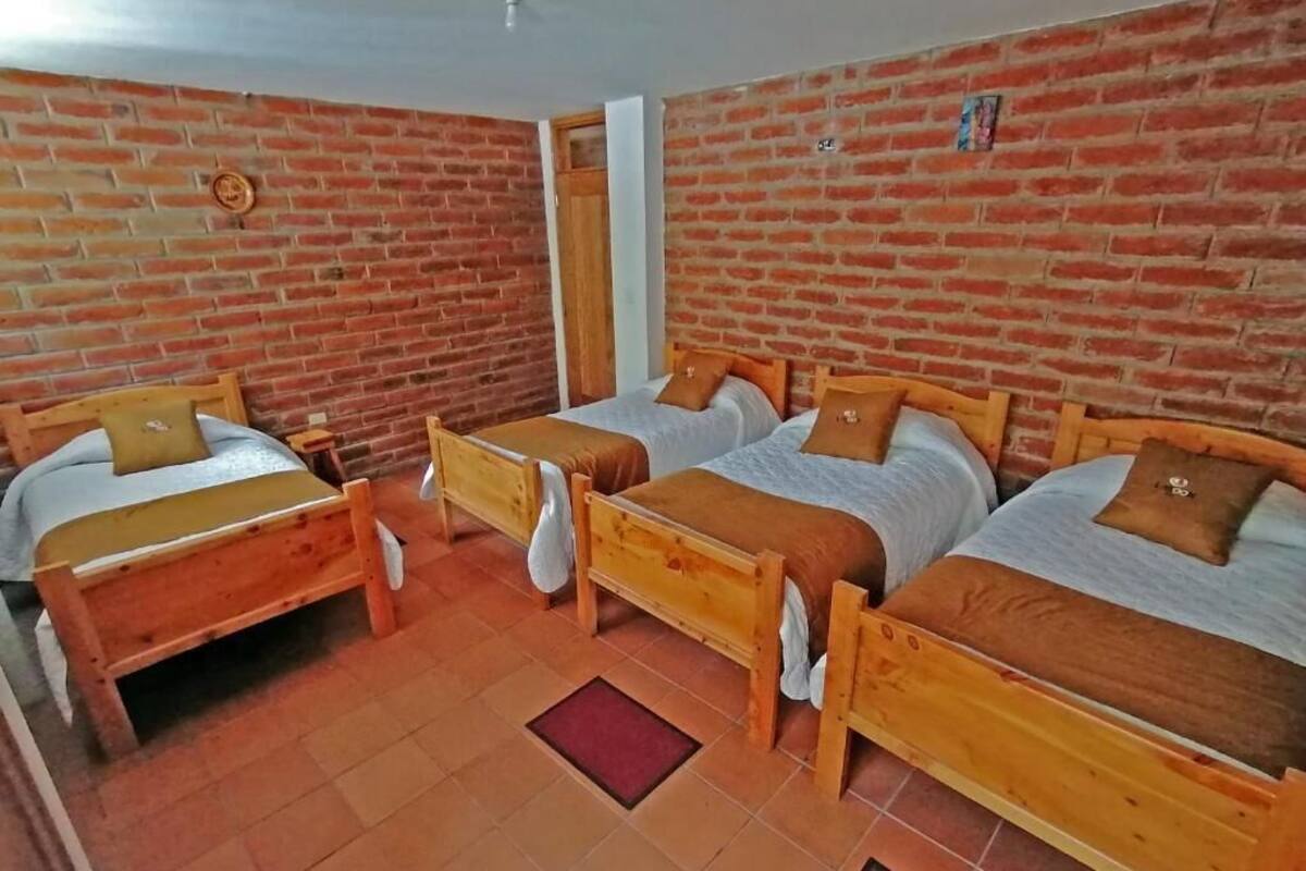 Ein Zimmer mit drei hölzernen Betten an Backsteinwänden, jeweils mit Kissen und Decke.