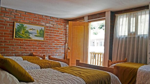 A room with two beds, a brick wall, a painting, and a balcony with a view. - LAGOON HOTEL (Chugchilan)