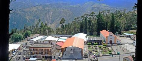 Un pueblo con una plaza central, edificios de techo rojo y un paisaje montañoso al fondo.