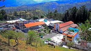 A town with a central plaza, buildings with red roofs, and a mountainous backdrop. - LAGOON HOTEL (Chugchilan)