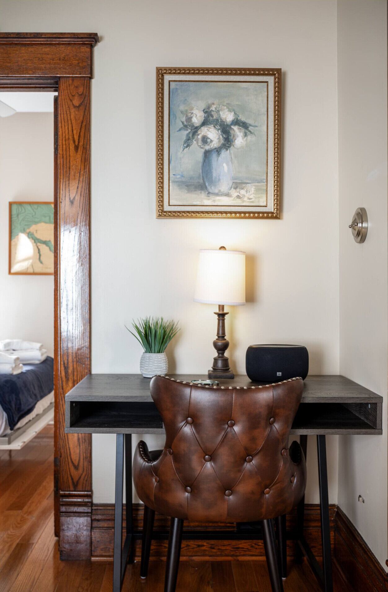 A dining area with a wooden table, a leather chair, a lamp, and a framed painting on the wall.