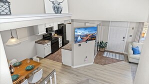 A modern apartment with a kitchen, dining area, and living room. It features a flat-screen TV, a white sofa, and a dining table set for four. - Chimney Park Retreat King Suite + Fenced Yard (Windsor)