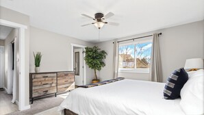 A bedroom with a bed, a ceiling fan, a window with curtains, a dresser, and a potted plant. - Chimney Park Retreat King Suite + Fenced Yard (Windsor)