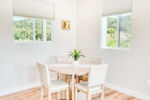 A dining area with a round table, four chairs, a potted plant, and two windows with blinds. - Edna Valley Modern Barndominium (Arroyo Grande)