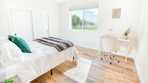 Ett sovrum med en säng, ett skrivbord och ett fönster med utsikt över grönområden.